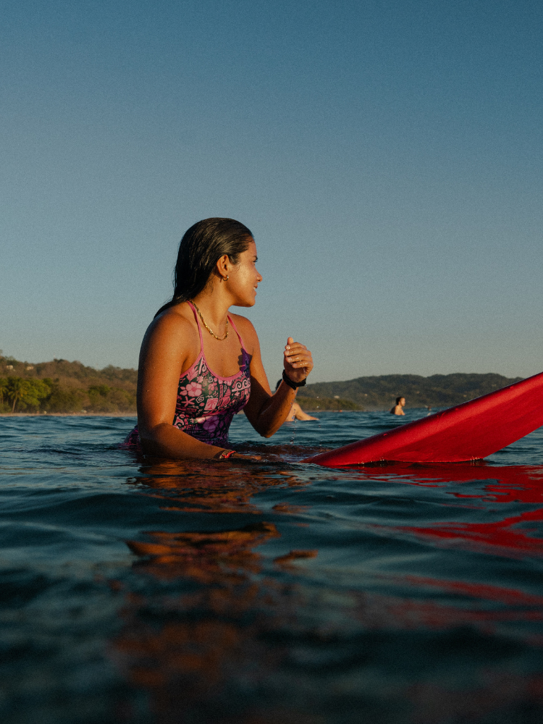 Women on a surf board out in the water wearing a pink and emerald green one piece surf suit 