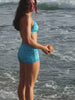 a women walking in the water while wearing a blue surf bikini top and matching blue surf shorts 
